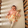 baby, crib, wooden_crib, toddler, dress, cardigan, tights, toy, stuffed_animal, blanket, indoor, sunlight, shadow, sleeping_area, child, cute, infant, person, soft_toy, relaxing