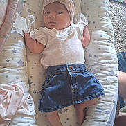 Lilana is registered to the contest to win money with this photo: baby, infant, headband, denim_skirt, white_top, cushion, star_pattern, lying_down, indoor, carpet, barefoot, small_feet, cute, person, child, soft_toys, baby_clothes, headwear, calm_expression, cozy