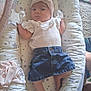 baby, infant, headband, denim_skirt, white_top, cushion, star_pattern, lying_down, indoor, carpet, barefoot, small_feet, cute, person, child, soft_toys, baby_clothes, headwear, calm_expression, cozy