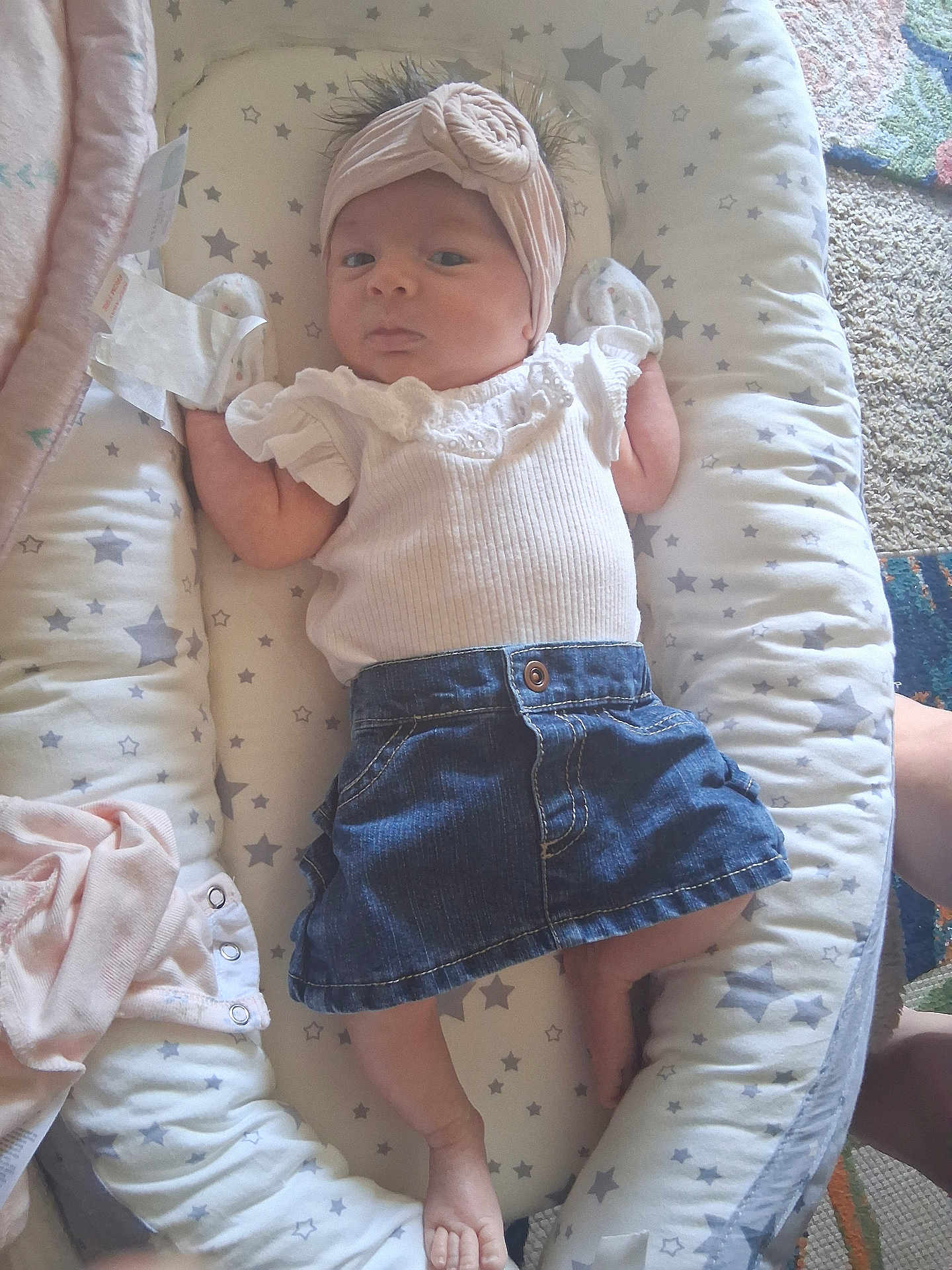 Lilana is registered to the contest to win money with this photo: baby, infant, headband, denim_skirt, white_top, cushion, star_pattern, lying_down, indoor, carpet, barefoot, small_feet, cute, person, child, soft_toys, baby_clothes, headwear, calm_expression, cozy