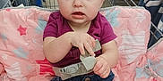 Samara is registered to the contest to win money with this photo: baby, shopping_cart, child, denim_skirt, purple_shirt, pink_blanket, safety_belt, curious_expression, blue_eyes, indoor, retail_store, clothing_rack, aisle, person, infant, cute, seated, holding, face, apparel