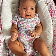 Alaska is registered to the contest to win money with this photo: baby, infant, onesie, floral_pattern, smile, cushion, bouncer, seat, happy, skin, hand, foot, face, head, child, clothing, indoors, fabric, cute, person