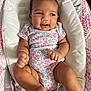 baby, infant, onesie, floral_pattern, smile, cushion, bouncer, seat, happy, skin, hand, foot, face, head, child, clothing, indoors, fabric, cute, person