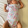 Alaska is registered to the contest to win money with this photo: baby, sleeping, infant, onesie, floral_pattern, white_sheet, cute, peaceful, skin, arms, legs, head, hair, newborn, soft_light, lying_down, child, indoors, natural_light, portrait