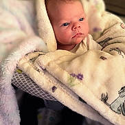 Andora is registered to the contest to win money with this photo: baby, blanket, infant, face, feet, cozy, patterned_blanket, indoor, child, wrapped, cute, newborn, soft_texture, warm, portrait, person, laying, expression, young, comfort