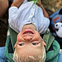 child, blonde_hair, smiling, toy, green_chair, white_shirt, outdoor, happy, portrait, casual_clothing, closeup, seat, playful, young_child, face, person, blue_eyes, holding, nature, daylight