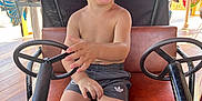 Soan a rejoint le concours — aidez-le/la à gagner de superbes lots ! toddler, child, boy, cap, shorts, shirtless, steering_wheel, ride_on_car, amusement_park, playful, smiling, seat, outdoor, sunlight, fun, toy, vehicle, happy, summer, casual