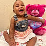 baby, child, smiling, denim_overalls, dress, teddy_bear, pink, heart, bed, blanket, happy, sitting, cute, portrait, indoor, person, toy, flower_pattern, infant, face