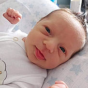 Luca joined the competition — help win amazing prizes! baby, newborn, infant, face, tongue_out, fist, onesie, white_clothing, pillow, star_pattern, closeup, cute, expression, child, skin, head, lying_down, indoors, soft_light, portrait