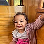 toddler, child, smiling, curly_hair, pink_skirt, cardigan, wooden_bench, indoor, happy, cute, portrait, clothing, person, face, sitting, baby, fashion, expression, young_child, casual