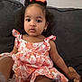 toddler, child, girl, dress, floral_pattern, bow, hair, earrings, couch, sofa, toy, wooden_toy, indoor, portrait, curious, sitting, young_child, casual_clothing, home, furniture