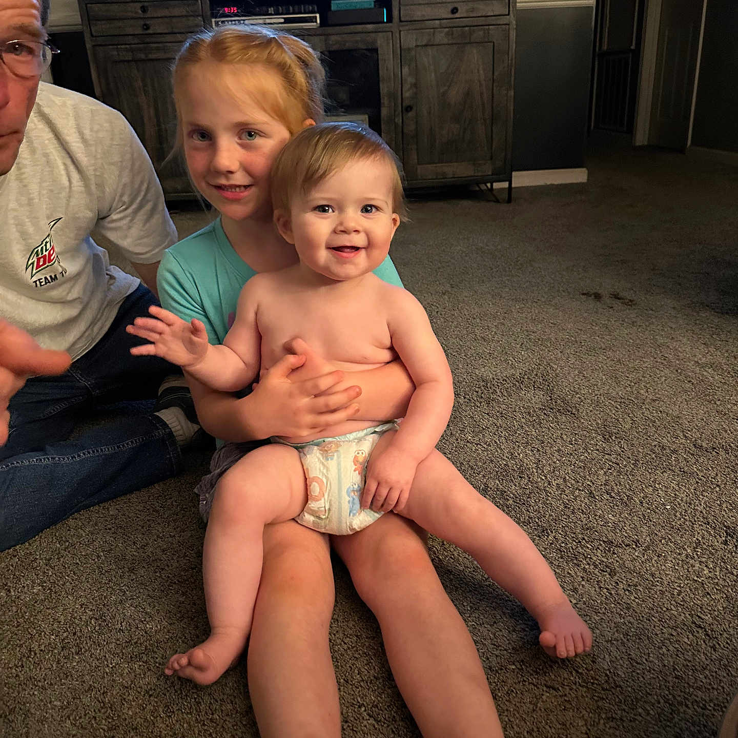 Oakley is registered to the contest to win money with this photo: baby, cabinet, candid, carpet, casual, child, diaper, family, floor, furniture, happy, home, indoor, light, people, person, room, sitting, smile, television