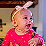 Evelyn joined the competition — help win amazing prizes! baby, infant, smile, pink_headband, bow, bright_clothing, happy, cute, child, portrait, indoor, person, hand, holding, cheeks, expression, eyes, warm_lighting, background_blur, closeup