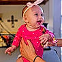 Evelyn is registered to the contest to win money with this photo: baby, infant, smiling, pink_outfit, headband, hands, indoor, kitchen, joyful, cute, child, person, holding, pacifier, accessory, human, happy, portrait, closeup, warm_lighting