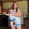 cabinet, casual_clothing, child, face, family, holding, home, indoor, long_hair, mop, motion_blur, rustic, shorts, smile, tank_top, toddler, water_jug, woman, wooden_floor, wooden_wall