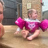 Dixie is registered to the contest to win money with this photo: baby, brick_wall, child, concrete, cute, expression, face, floaties, fun, gate, outdoor, parent, person, pink, play, sitting, summer, swimwear, water, wet
