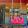child, concrete_floor, cord, daylight, door, orange_feet, outdoor, person, pink_swing, play, porch, rope, rustic, seat, smiling, swing, toddler, tools, window, wooden_wall