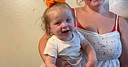 Dixie is registered to the contest to win money with this photo: baby, casual_clothing, child, family, fun, happy, holding, home, indoor, jeans, joy, motion_blur, orange_bow, person, portrait, smile, toddler, white_top, woman, young_adult