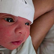 Uriah joined the competition — help win amazing prizes! newborn, baby, infant, child, portrait, close_up, face, eyes, wide_eyed, white_hat, knit_cap, white_clothing, swaddled, cradled, adult_arm, indoors, cozy, sleepwear, photography, cute