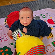 Rhydian is registered to the contest to win money with this photo: baby, child, infant, plush_toy, play_mat, colorful, face, eyes, clothing, floor, wooden_floor, pattern, soft_toy, toddler, indoor, person, cute, lying, hand, expression