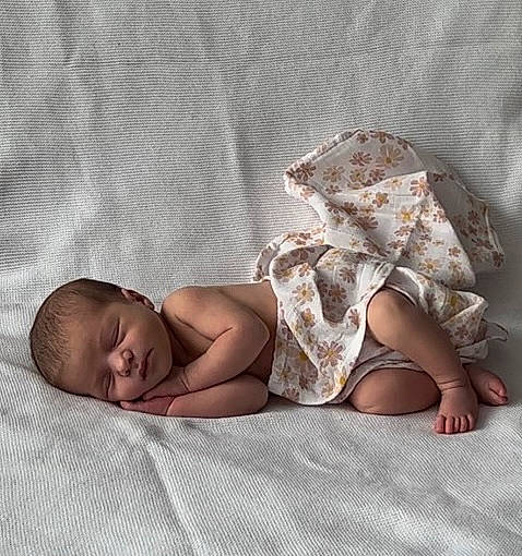 Kamila participe au concours pour gagner de l'argent avec cette photo : arm, baby, baby_toddler_clothing, barefoot, bed, bedding, comfort, face, facial_expression, foot, hand, head, human_body, human_leg, linens, pattern, person, skin, sleeve, thigh
