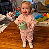 toddler, child, pink_outfit, toy, watering_can, wooden_floor, living_room, couch, person, smile, curly_hair, indoor, playtime, shoes, blanket, stuffed_toy, carpet, window, furniture, happy