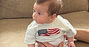 Cosmo is registered to the contest to win money with this photo: baby, infant, child, person, couch, sofa, furniture, hand, clothing, shirt, flag, american_flag, sitting, indoor, portrait, looking_away, skin, hair, cozy, casual