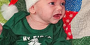Christian joined the competition — help win amazing prizes! baby, celebration, child, christmas, colorful_background, cute, festive, green_shirt, happy, holiday, holiday_clothing, indoors, infant, patchwork_quilt, patterned_pants, portrait, red_hat, santa_hat, smiling, white_fur_trim