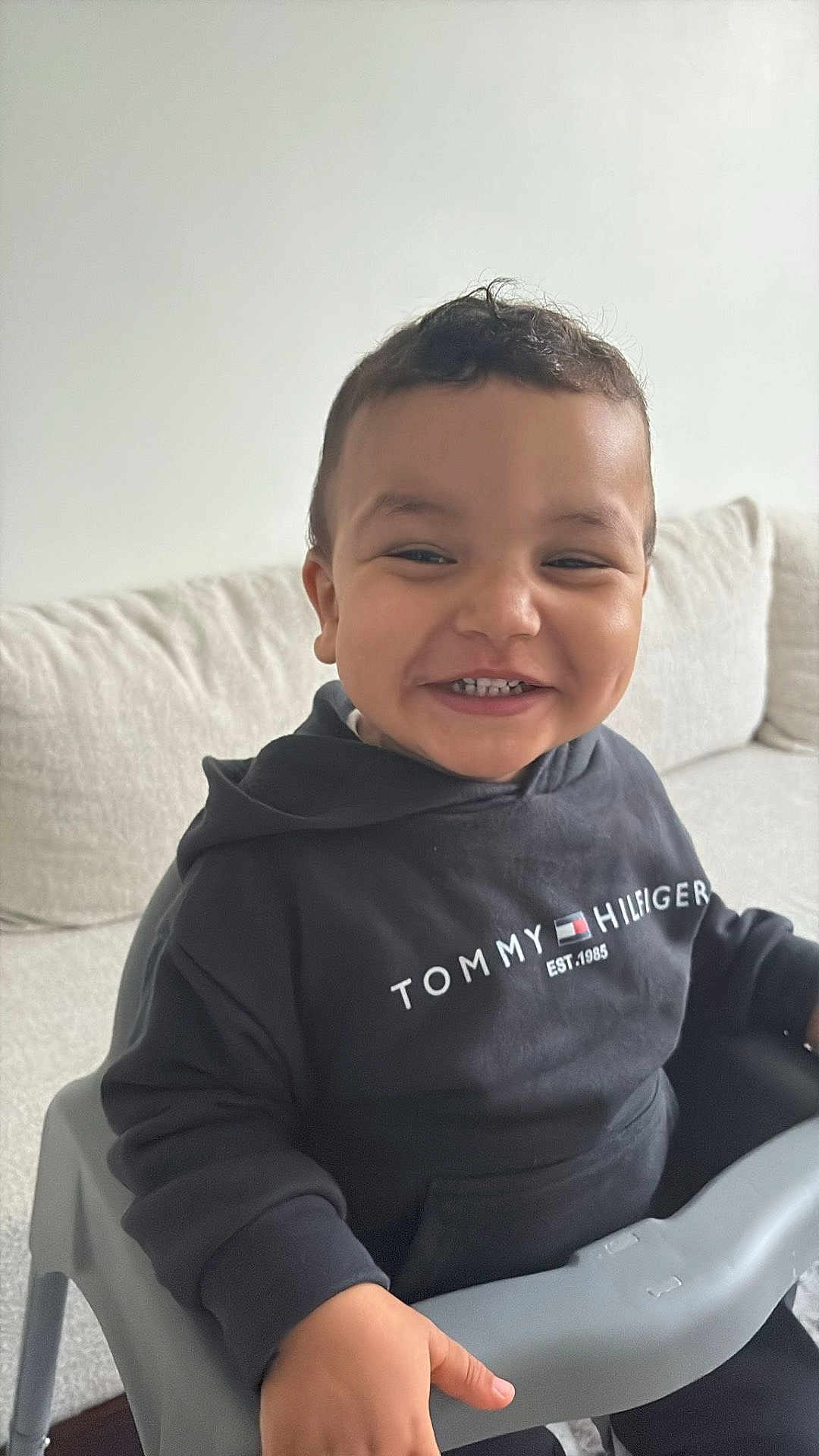 Adam a rejoint le concours — aidez-le/la à gagner de superbes lots ! toddler, child, smiling, high_chair, black_hoodie, tommy_hilfiger, indoor, couch, person, happy, sitting, young_child, furniture, face, casual_clothing, home, cute, portrait, hand, short_hair
