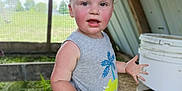 Bobby Ray is registered to the contest to win money with this photo: toddler, child, boy, gray_shirt, dinosaur_print, outdoor, rustic, bucket, grass, fence, curious, rosy_cheeks, hands, blurry_background, daylight, portrait, casual_clothing, nature, young_child, playful