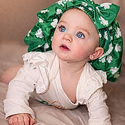 Echo joined the competition — help win amazing prizes! baby, blue_eyes, green_bonnet, white_clovers, bow, white_outfit, ruffles, droplet, curious_expression, lying_down, soft_surface, infant, cute, portrait, indoor, child, face, headwear, adorable, closeup