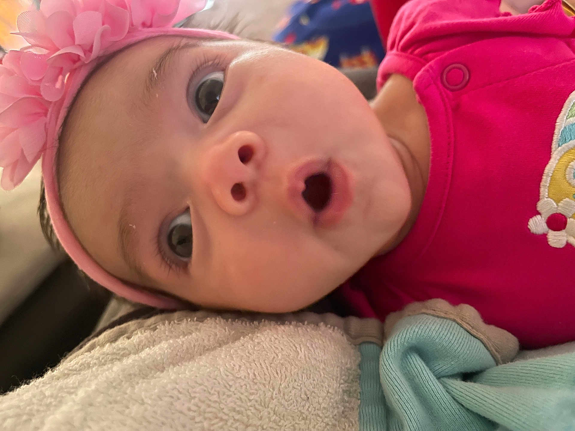 Mia joined the competition — help win amazing prizes! baby, closeup, face, headband, pink, flower, expression, surprised, eyes, mouth, towel, blanket, clothing, infant, cute, portrait, skin, person, lying_down, indoors