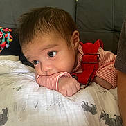 Mia is registered to the contest to win money with this photo: baby, infant, face, arm, red_overalls, striped_shirt, blanket, animal_print, couch, indoor, curious, wide_eyes, resting, soft_texture, closeup, child, person, young, head, hand