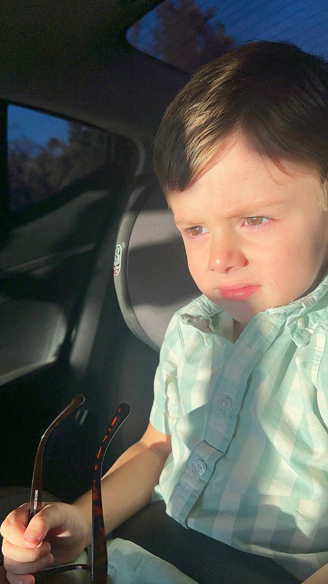 Leonel is registered to the contest to win money with this photo: child, boy, car_seat, sunglasses, sunlight, serious_expression, short_hair, casual_clothing, window, car_interior, seatbelt, daylight, portrait, young, light_and_shadow, holding, face, person, indoors, seat