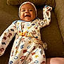 baby, infant, smiling, onesie, cowboy_theme, hat, couch, brown, fabric, comfort, happy, child, cute, pacifier_clip, raised_hand, portrait, indoors, relaxed, playful, young