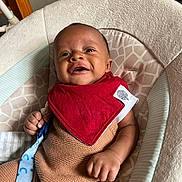 Atticus is registered to the contest to win money with this photo: baby, infant, smiling, red_bib, knit_outfit, baby_chair, cushion, indoor, happy, person, child, seat, cute, clothing, hand, face, portrait, comfort, young, relaxed