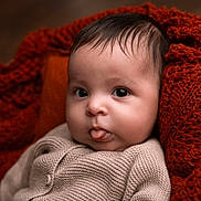 Aylan participe au concours pour gagner de l'argent avec cette photo : baby, infant, face, tongue, knit_sweater, cozy, blanket, orange_blanket, close_up, cute, child, portrait, soft_skin, warm_colors, indoors, newborn, expression, curious, small_person, sitting