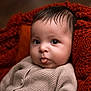baby, infant, face, tongue, knit_sweater, cozy, blanket, orange_blanket, close_up, cute, child, portrait, soft_skin, warm_colors, indoors, newborn, expression, curious, small_person, sitting