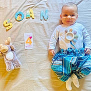 Soän participe au concours pour gagner de l'argent avec cette photo : baby, infant, child, plush_toy, moose_toy, letters, soan, card, age_card, clothing, pants, white_shirt, sock, bed, blanket, smile, face, milestone, lying_down, cute