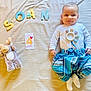 age_card, baby, bed, blanket, card, child, clothing, cute, face, infant, letters, lying_down, milestone, moose_toy, pants, plush_toy, smile, soan, sock, white_shirt