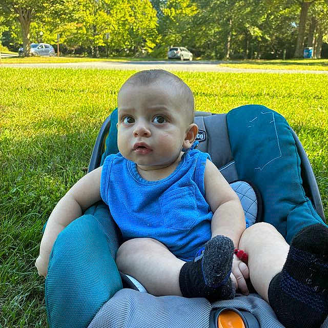 Joseph Escobar is registered to the contest to win money with this photo: baby, blue_shirt, car_seat, child, curious, daytime, grass, greenery, infant, nature, outdoor, parked_car, person, relaxed, seat, socks, summer, sunlight, trees, young_child