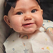 Riley is registered to the contest to win money with this photo: baby, child, smiling, headband, black_bow, bib, rainbow, stars, high_chair, book, toy, face, cheeks, cute, indoor, infant, person, happy, clothing, portrait