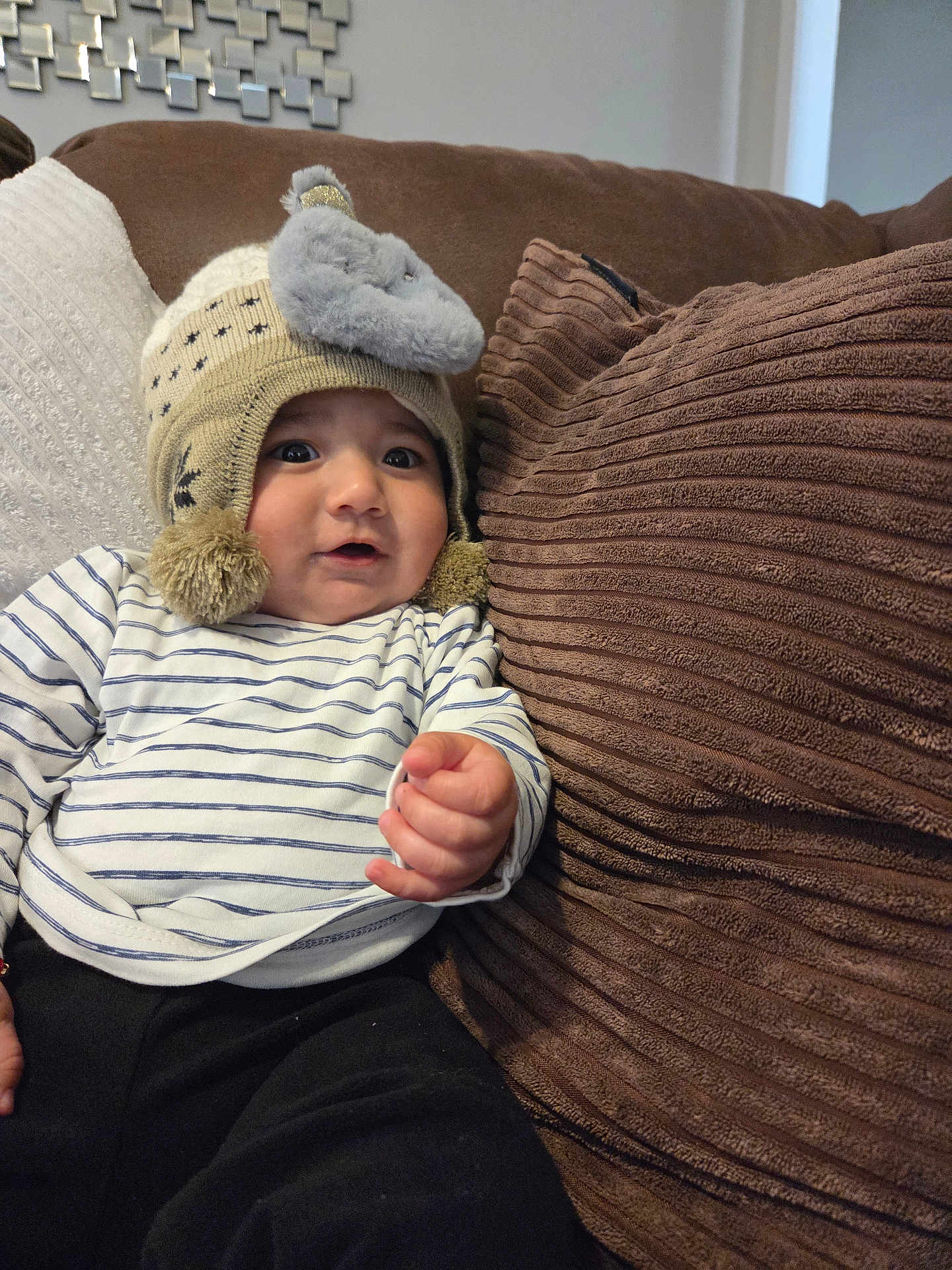 Enzo joined the competition — help win amazing prizes! baby, child, hat, knitted_hat, elephant, plush, striped_shirt, couch, pillow, brown_pillow, white_pillow, indoor, cozy, soft, curious, person, infant, casual_clothing, hand, smiling