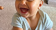 Jude is registered to the contest to win money with this photo: baby, child, smiling, laughing, portrait, indoors, living_room, carpet, seated, crawling, short_hair, blue_shirt, bracelet, hands, face, teeth, happy, family, home, photography