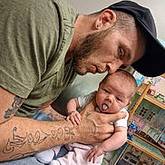 Taileah is registered to the contest to win money with this photo: man, baby, tattoo, cap, tongue_out, indoor, dollhouse, furniture, can, beverage, person, child, holding, clothing, casual, facial_expression, home, seated, hand, cute