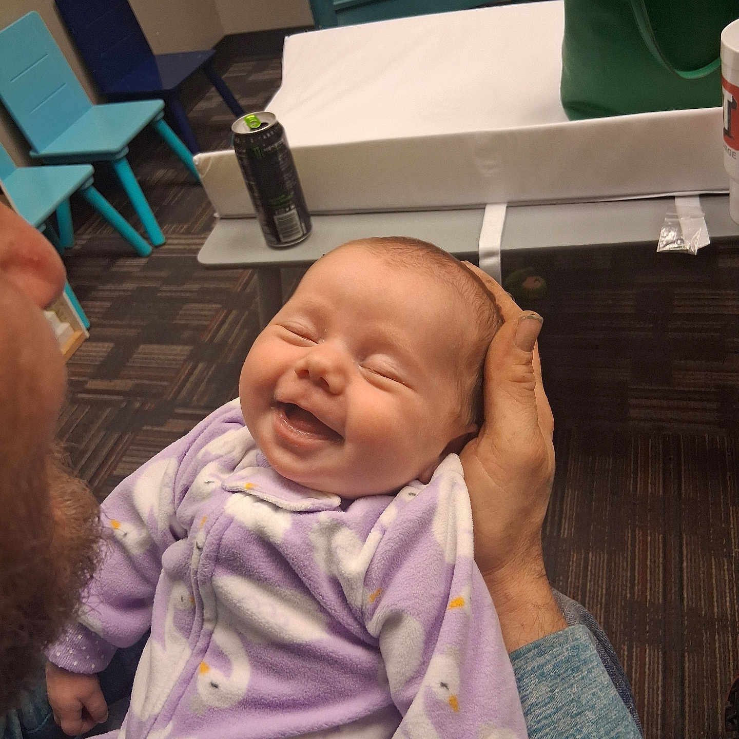 Taileah joined the competition — help win amazing prizes! adult, baby, beard, carpet, chairs, cozy, cute, energy_drink, face, green_bag, hand, happy, indoor, infant, person, purple_onesie, smiling, swan_pattern, table, white_pad