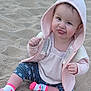 baby, child, sand, hoodie, pink, socks, leggings, playful, tongue_out, cute, outdoor, sitting, smiling, face, person, clothing, casual, young_child, happy, funny_expression