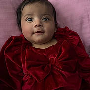 Naina is registered to the contest to win money with this photo: baby, bow, child, closeup, cute, face, happy, head, indoors, infant, lying_down, person, pink_background, portrait, red_clothing, sleepwear, smile, soft_fabric, velvet, young_child