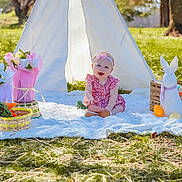 Wrenley is registered to the contest to win money with this photo: baby, child, outdoor, grass, blanket, teepee, tent, flower_bouquet, basket, toy, carrot, headband, pink_dress, easter_eggs, bunny_figure, spring, sunny, smiling, sitting, playtime