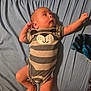 baby, bear_face, bed, blanket, blue_sheet, curious, cute, foot, hand, indoors, infant, lying_down, newborn, onesie, person, portrait, raised_arm, skin, sleepwear, striped_clothing